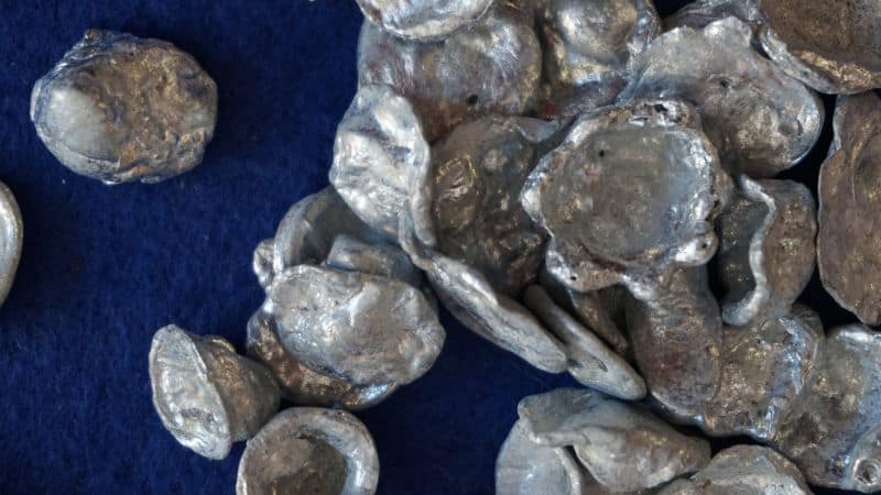 Close-up of ancient silver coins with various shapes and imprints on a dark blue background.