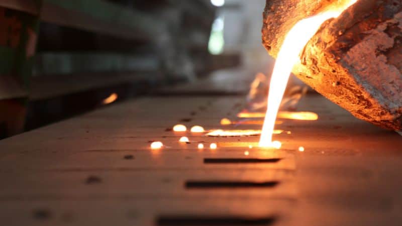 Molten metal pours from a large container into molds on an industrial production line.