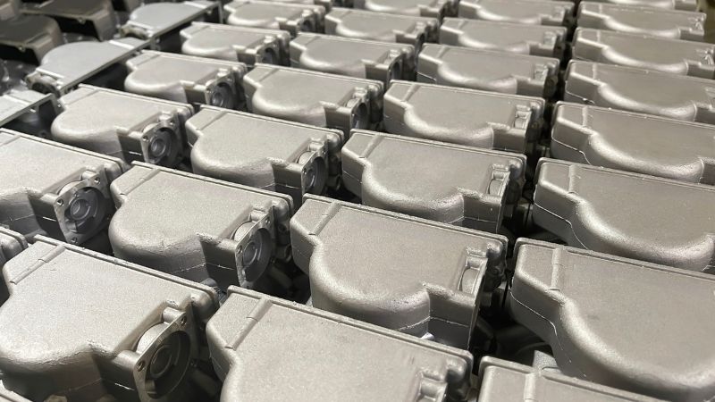 Piezas fundidas de metal plateado idénticas están perfectamente alineadas en una cuadrícula, lo que sugiere una producción en masa en un entorno industrial.