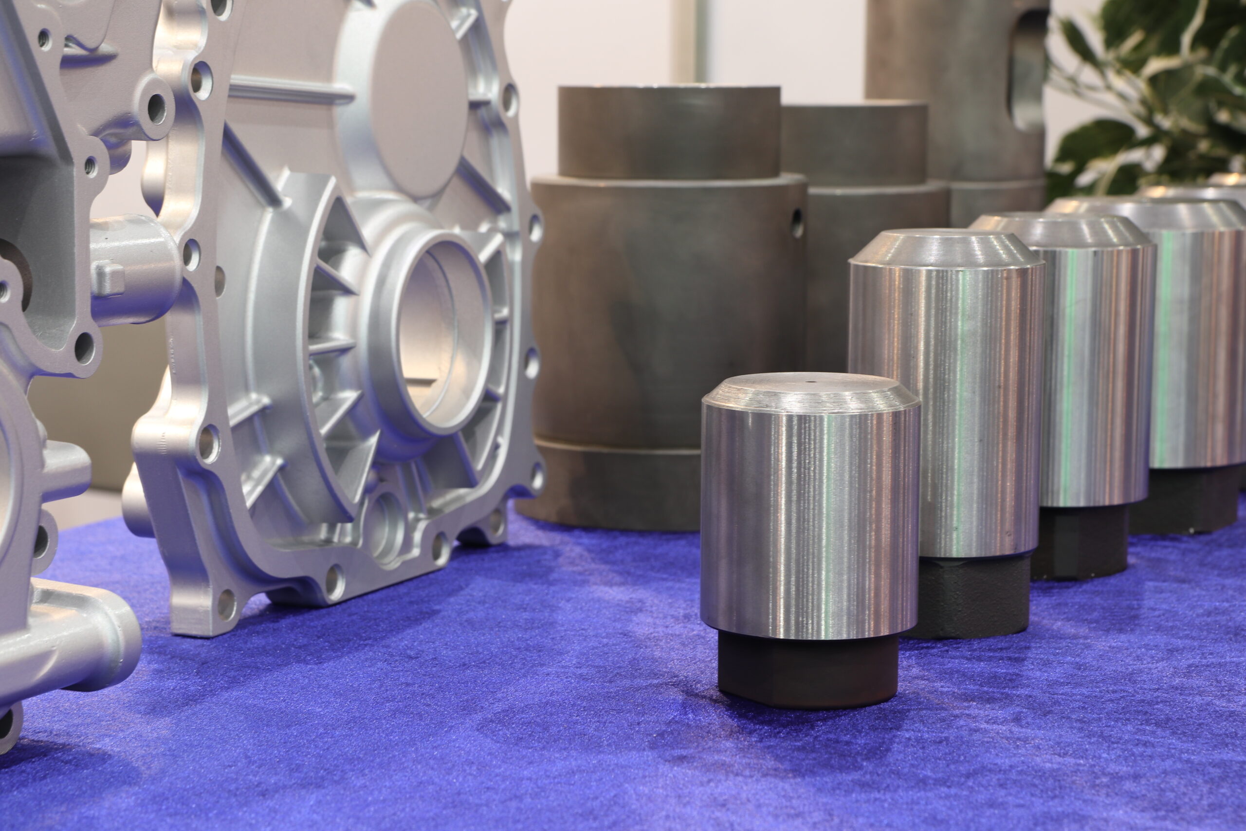 Metal machine parts, including cylinders and a large gear housing, on blue fabric.