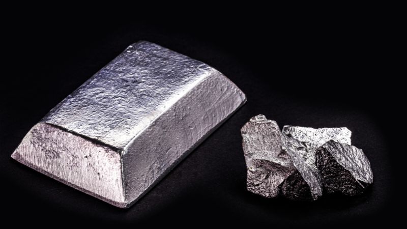 A zinc ingot and several rough ore pieces rest on a black background.