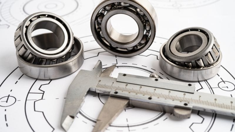 Metal bearings and a caliper rest on technical drawings with circular mechanical designs.