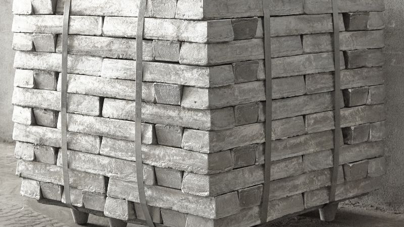 magnesium metal bars, strapped with two metal bands, sit stacked on a wooden pallet.