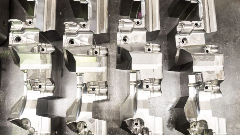 Multiple metal die cast parts arranged on a metallic surface, showcasing precision manufacturing for scalable metal component production.