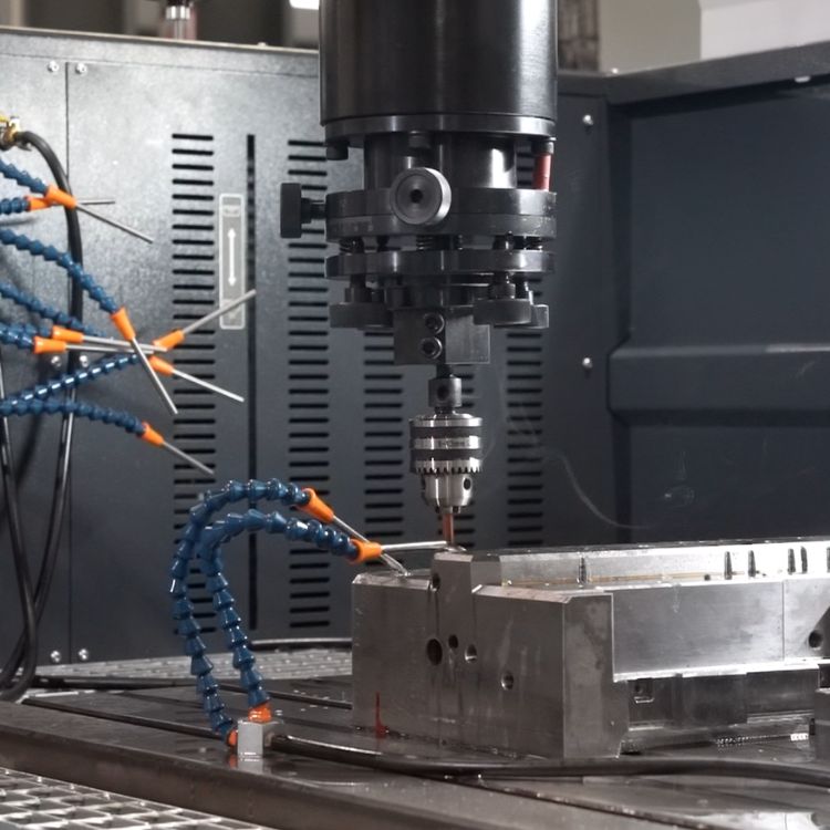 Close-up of CNC machine performing precision machining on a metal mold with multiple coolant hoses in a manufacturing setting.