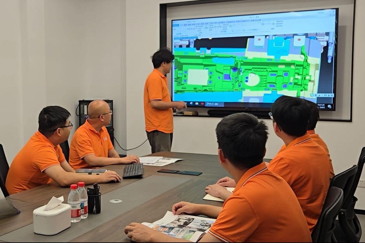 Team of engineers reviewing a 3D mold design on a large screen in a modern conference room.